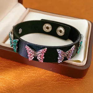 Détail d'un bracelet en cuir noir avec des breloques papillon en strass colorés.