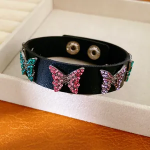 Détail d'un bracelet en cuir noir avec des papillons scintillants en strass colorés