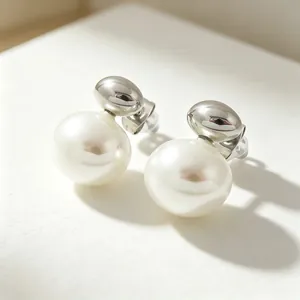 Macro detail of minimalist stainless steel stud earrings with white shell pearl drop