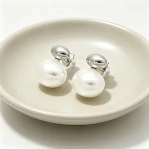 Detailed view of minimalist silver stud earrings with large white shell pearls on a tray