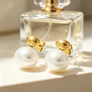 Detailed close-up of minimalist gold oval earrings with large white pearls on a stone surface