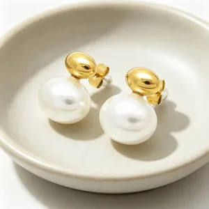 Close-up of elegant gold stainless steel earrings with white pearls in a ceramic dish