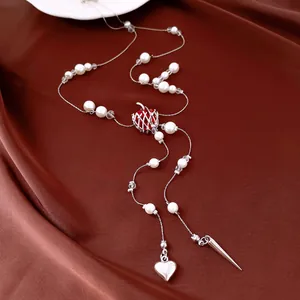 Détail d'un collier en perles avec pendentif pomme rouge et gland cœur sur tissu satiné