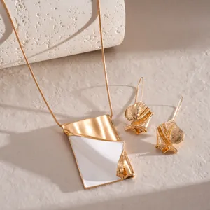 Macro view of gold-toned jewelry set featuring white enamel folded book pendant