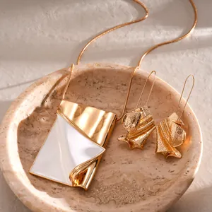 Detail shot of a gold-toned folded book pendant necklace and textured earrings set