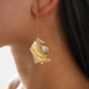 Close-up detail of artistic gold metal hook earring with abstract folded page design