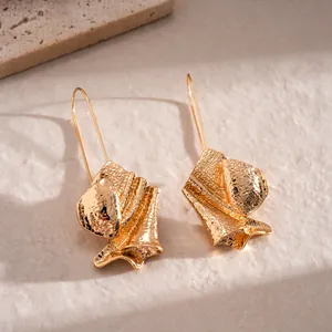 Detailed view of elegant gold irregular textured leaf earrings on a stone surface