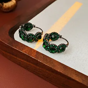Détail rapproché de créoles de style palais rétro avec des zircons verts scintillants