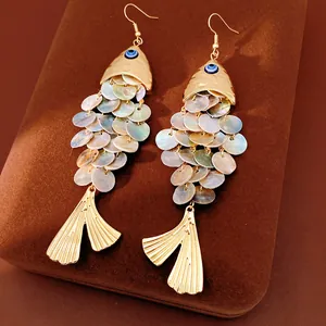 Détail de boucles d'oreilles poisson vintage avec écailles en nacre et œil bleu sur velours.