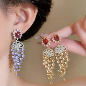 Detail of luxury 18k gold plated earrings with red gems and grape-like bead tassels