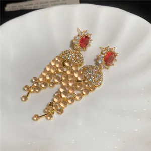 Close-up of 18k gold plated tassel earrings with red zircon and orange beads.