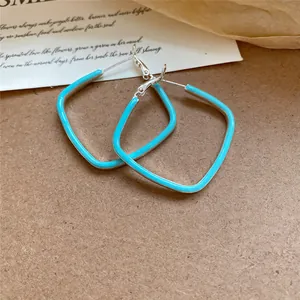 Gros plan détaillé de boucles d'oreilles créoles losanges en émail turquoise éclatant.