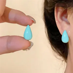 Détail d'une boucle d'oreille goutte en émail bleu clair tenue et portée sur l'oreille