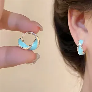 Détail de créoles torsadées en émail bleu montrées tenues et portées.
