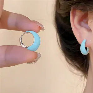 Détail rapproché de créoles en émail cyan montrant la texture lisse et l'effet porté