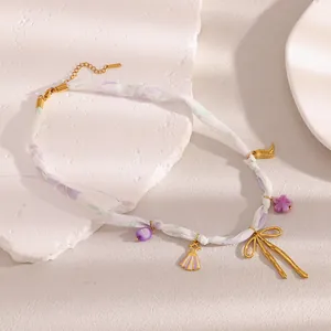 Detailaufnahme einer lila geblümten Bandhalskette mit einem großen goldenen Schleifenanhänger