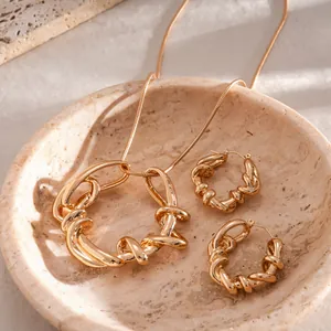 Détail d'un ensemble collier et boucles d'oreilles géométriques torsadés dorés.