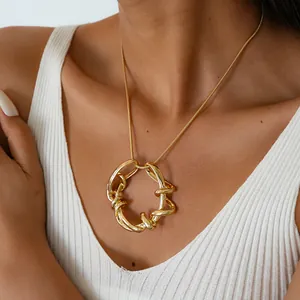 Gros plan d'un collier géométrique doré entrelacé sur un débardeur blanc côtelé