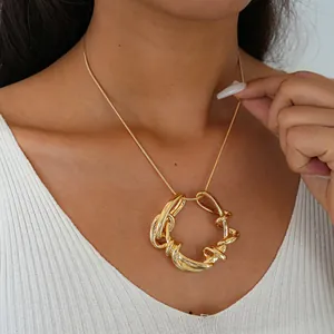 Gros plan d'un collier doré avec un pendentif géométrique entrelacé irrégulier sur un mannequin.