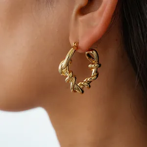 Gros plan d'une boucle d'oreille créole géométrique dorée avec un design torsadé