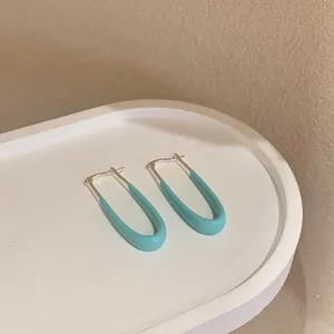 Dettaglio di orecchini geometrici in smalto blu chiaro su un vassoio bianco ovale
