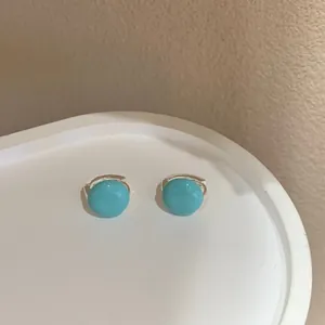 Primo piano di orecchini a cerchio minimalisti in smalto azzurro su un supporto bianco curvo