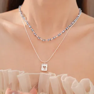 Detailopname van een dubbele ketting met blauwe kralen en zilveren hartjes hanger