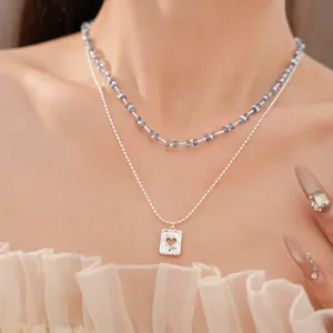 Detailopname van een gelaagde ketting met blauwe kralen en hartjeshanger gedragen door model