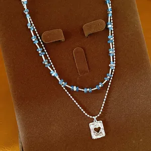 Detailweergave van een dubbellaagse halsketting met blauwe kralen en hartjes hanger.