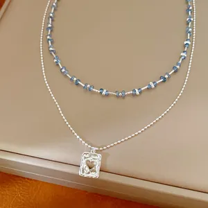 Detail van de zilveren dubbellaagse ketting met blauwe kralen en hartvormige hanger