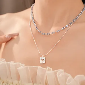 Gedetailleerde close-up van een dubbellaagse ketting met blauwe kralen en een hart