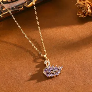 Primo piano di una collana con ciondolo a cigno con zirconi viola e catena dorata.