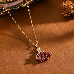 Dettaglio di una collana con ciondolo a cigno dorato con eleganti zirconi rossi marquise.