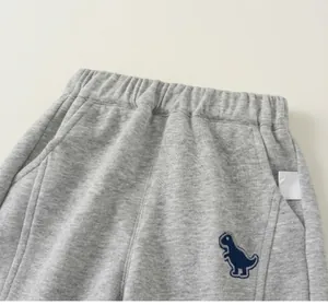 Détail d'un pantalon de jogging gris pour enfant avec taille élastique et écusson dinosaure