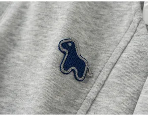 Zoom sur l'écusson dinosaure bleu tricoté sur ce pantalon de jogging gris pour enfant