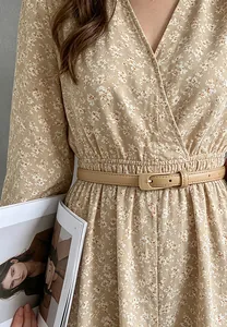 Détail d'une fine ceinture en cuir PU beige avec boucle ardillon sur robe à fleurs