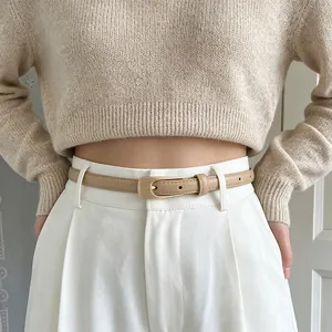 Détail d'une ceinture fine en PU beige avec boucle dorée vintage sur un pantalon blanc
