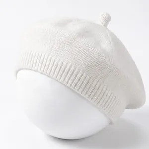 Close-up of a white knitted baby beret featuring soft textured yarn and top stem detail.