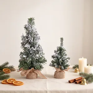 Miniature artificial snow-sprayed Christmas tree with burlap base in festive setting