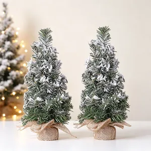 A pair of mini snow-flocked artificial Christmas trees with burlap bases for desk