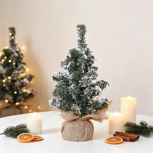 Miniature frosted Christmas tree with snow spray and burlap base on white table for decoration