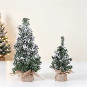 Detail view of two tabletop artificial snow Christmas trees with rustic burlap bases