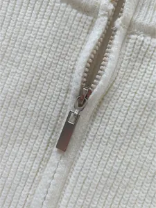 Macro view of a durable silver metal zipper on premium white ribbed knit cardigan fabric