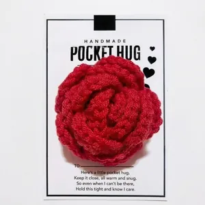 Close-up of handmade red crocheted rose pocket hug gift with white sentiment card