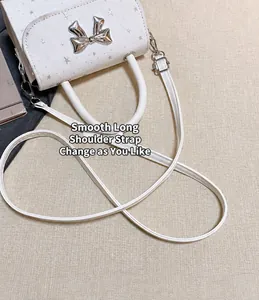 Detailed view of a stylish white shoulder bag featuring a silver bow and long strap