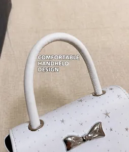 Close-up of the elegant bow detail and round handle on a white star-patterned handbag.