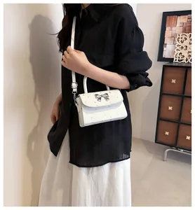 Stylish white crossbody bag with silver bow detail worn by model in casual setting