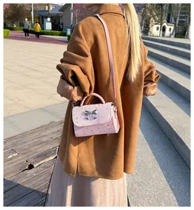 Stylish pink crossbody bag with silver bow accent, shown in a lifestyle outdoor setting.
