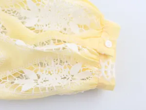 Détail de la broderie florale évidée blanche et du bouton sur chemisier jaune