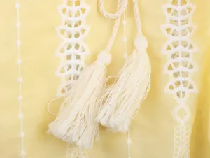 Gros plan sur les broderies blanches et les glands d'un chemisier jaune de style français.